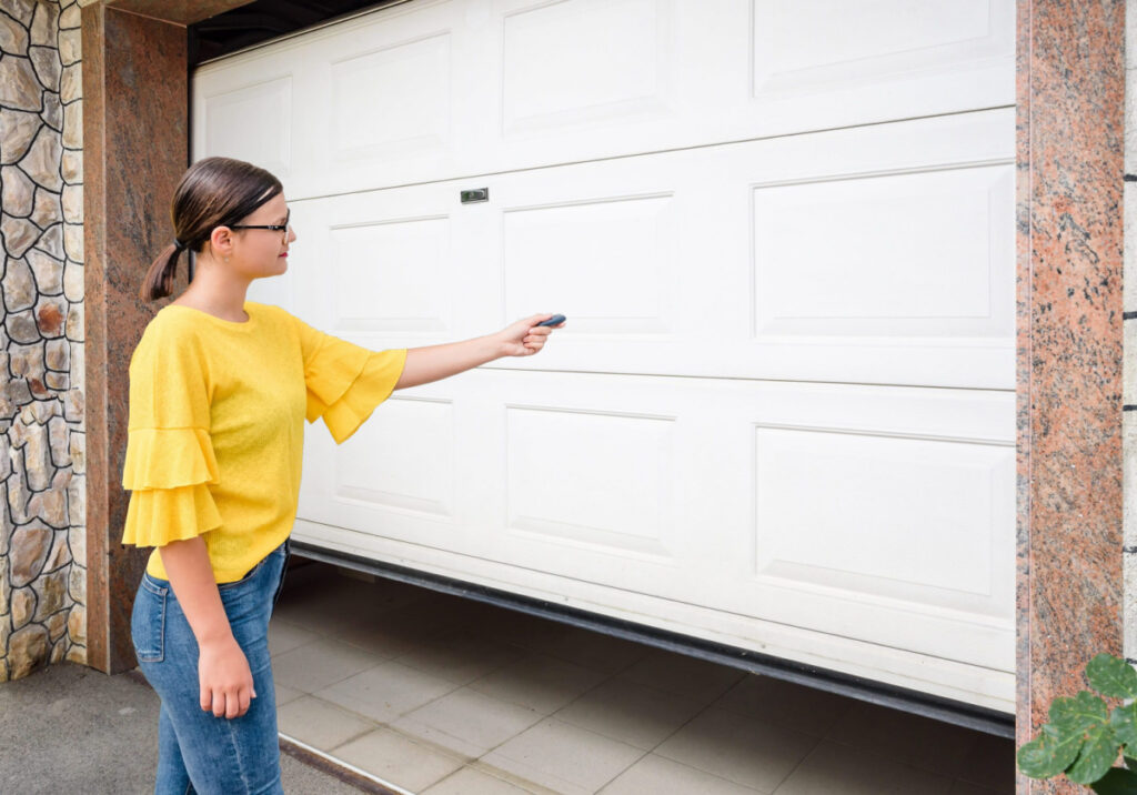 A woman using a garage door opener remote to open a garage door.